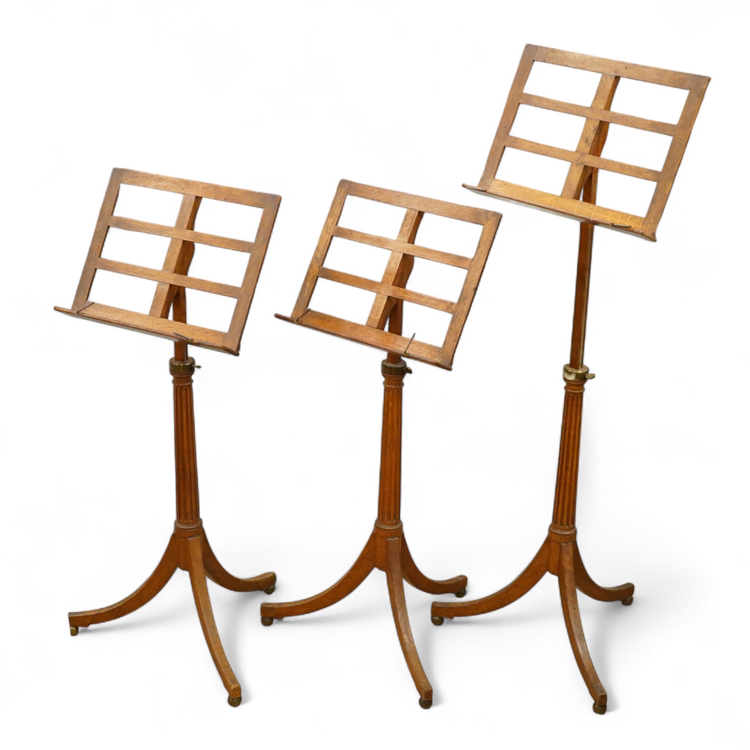 A set of three early 20th century oak music stands, all with fluted pedestal supports and tripod legs with brass feet, adjustable height music desks, maximum overall height when extended 137cm, the angle of the desks is